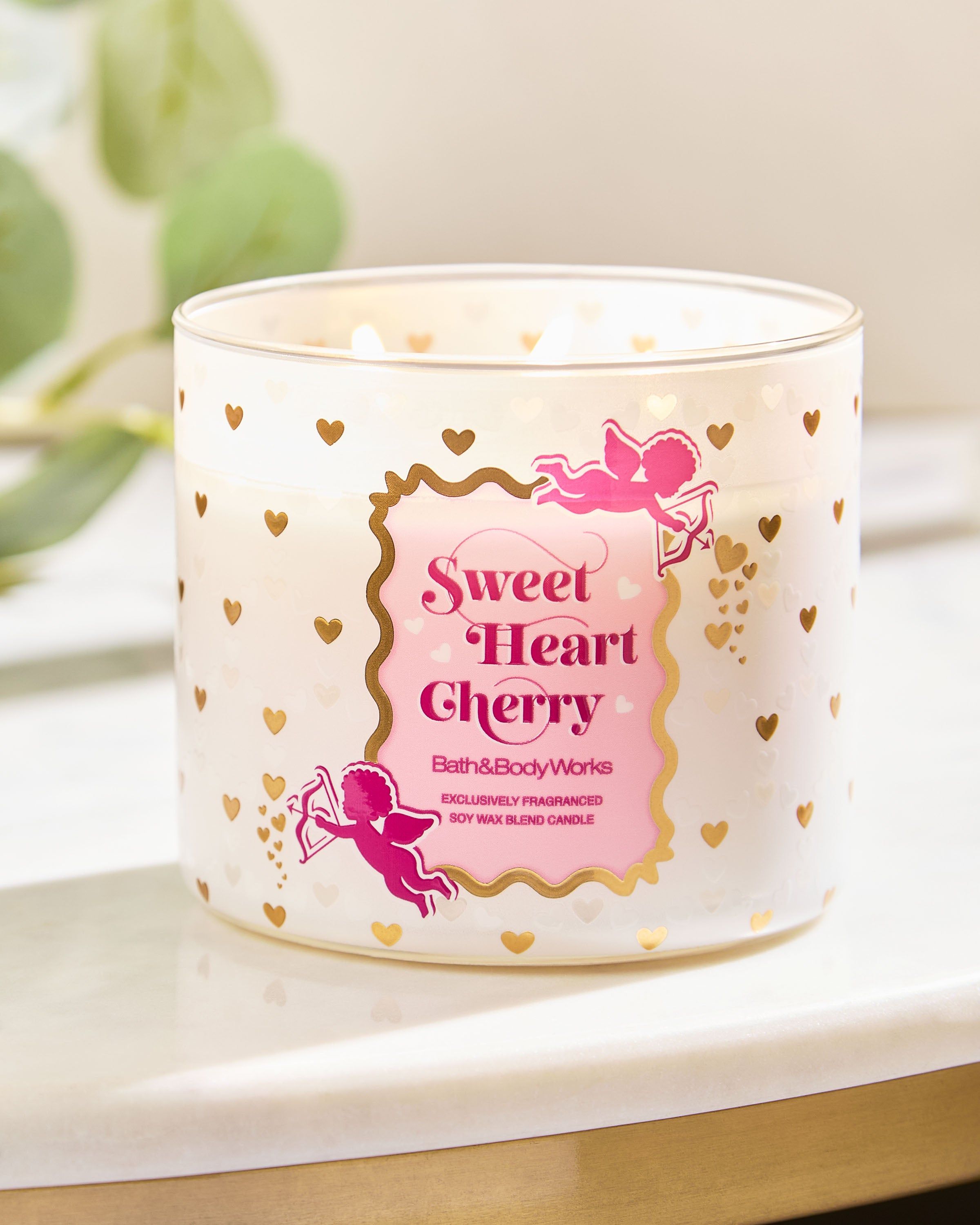 Lumânarea Sweet Heart Cherry cu logo roz și inimioare aurii, așezată pe o suprafață luminoasă.