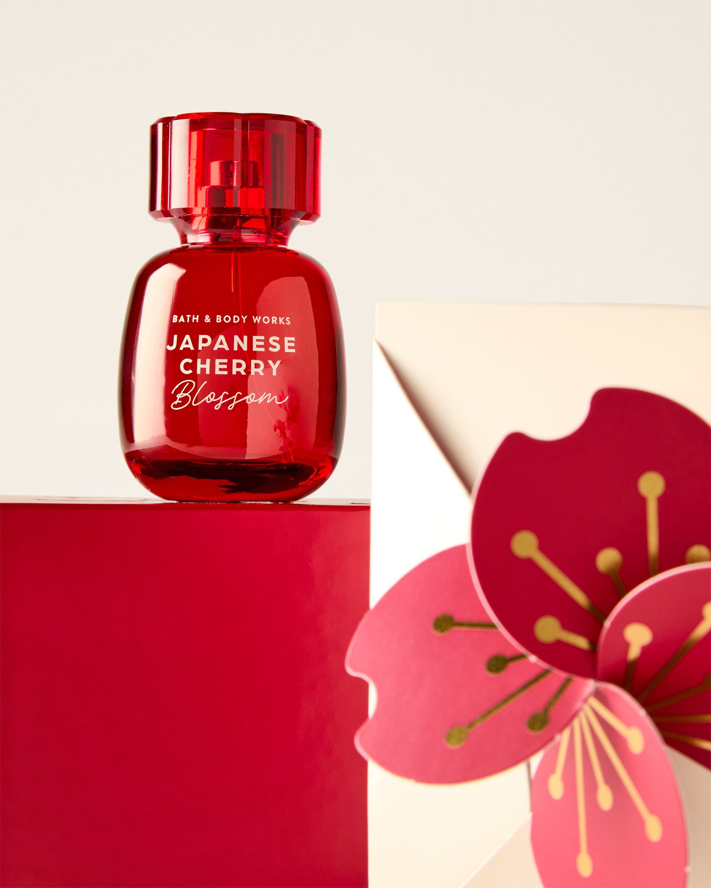 Apă de parfum Bath & Body Works Japanese Cherry Blossom în flacon roșu pe suport roșu cu element floral