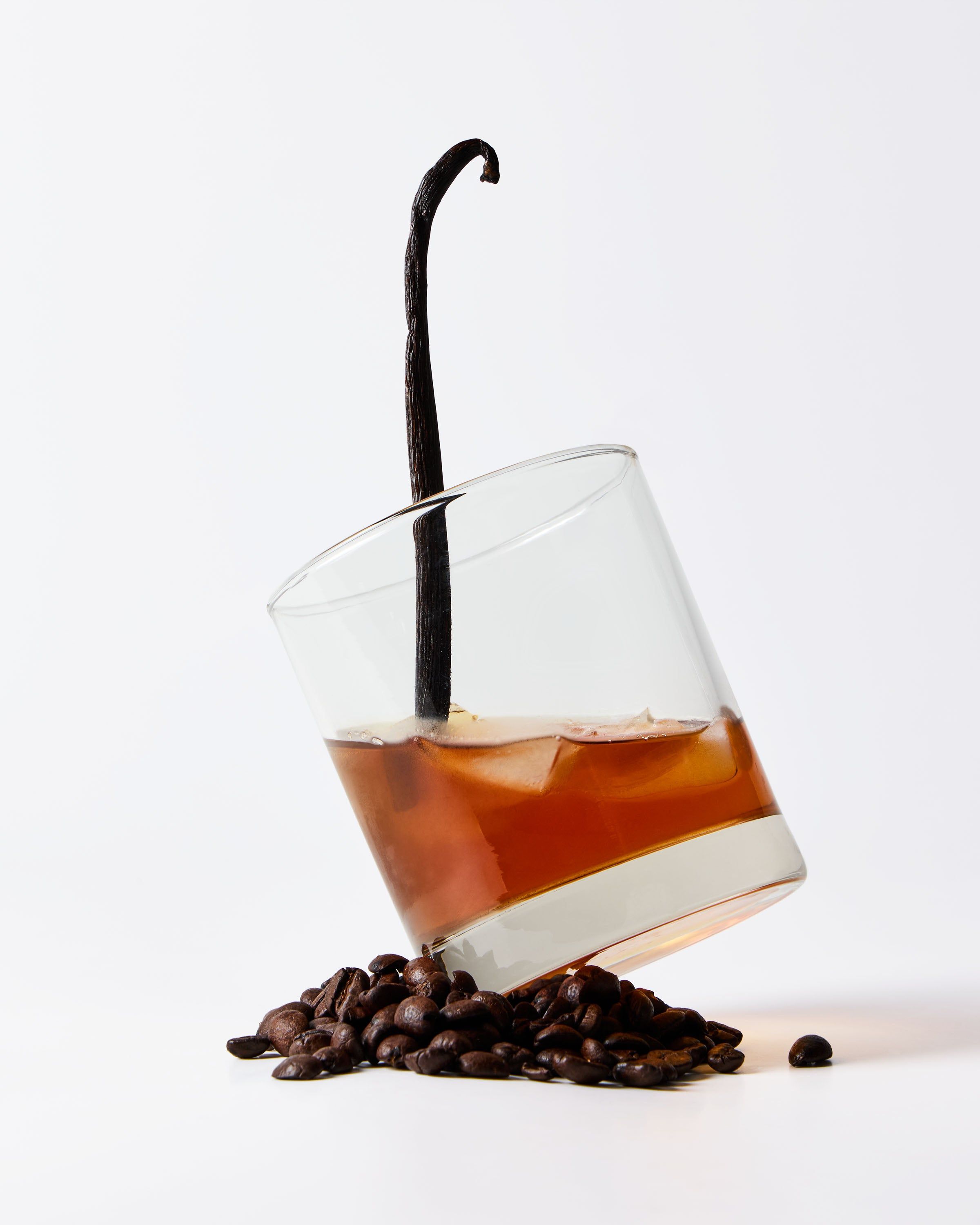 Păstaie de vanilie, boabe de cafea și băutură chihlimbarie într-un pahar pe fundal deschis