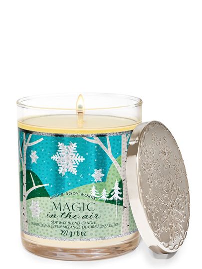 Vonné svíčky „Magic in the Air” s etiketou s motivem zimního lesa a sněhových vloček, Bath & Body Works.