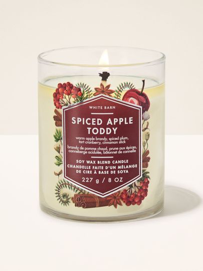 Lumânare parfumată Spiced Apple Toddy White Barn cu un fitil aprins și motiv de mere și scorțișoară