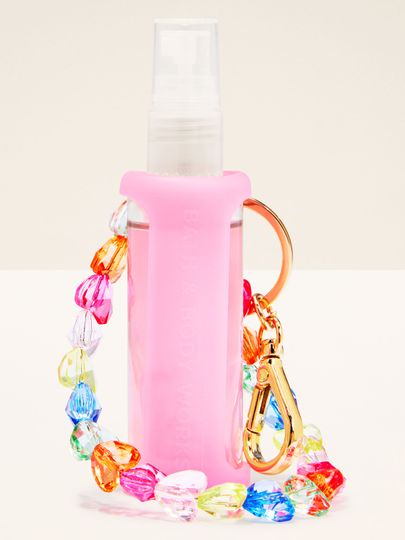 Suport roz pentru spray cu brățară colorată și carabină aurie, perfect pentru agățat la chei sau geantă.