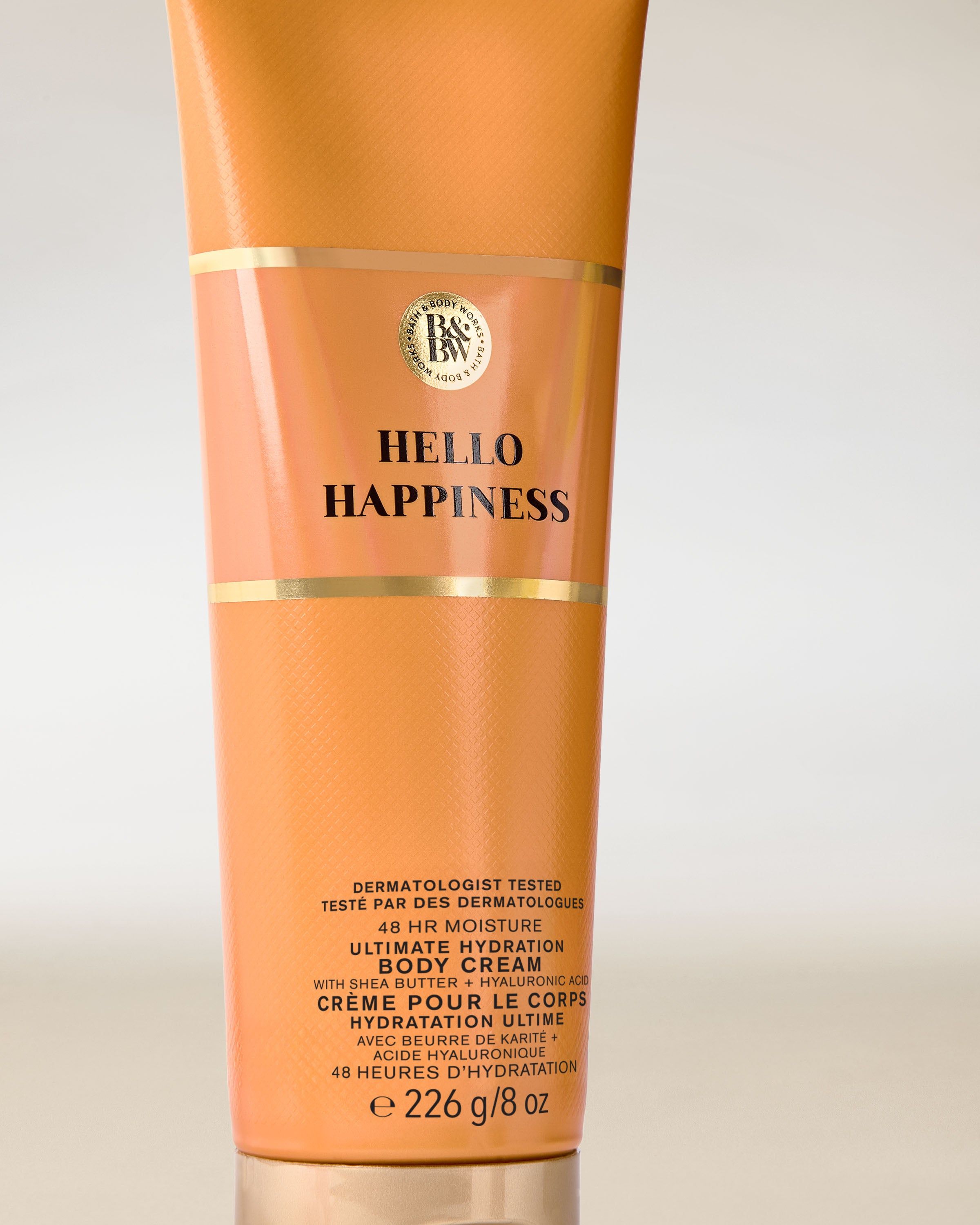 Cremă de corp Hello Happiness Bath & Body Works în tub portocaliu cu accente aurii, plină de energie.
