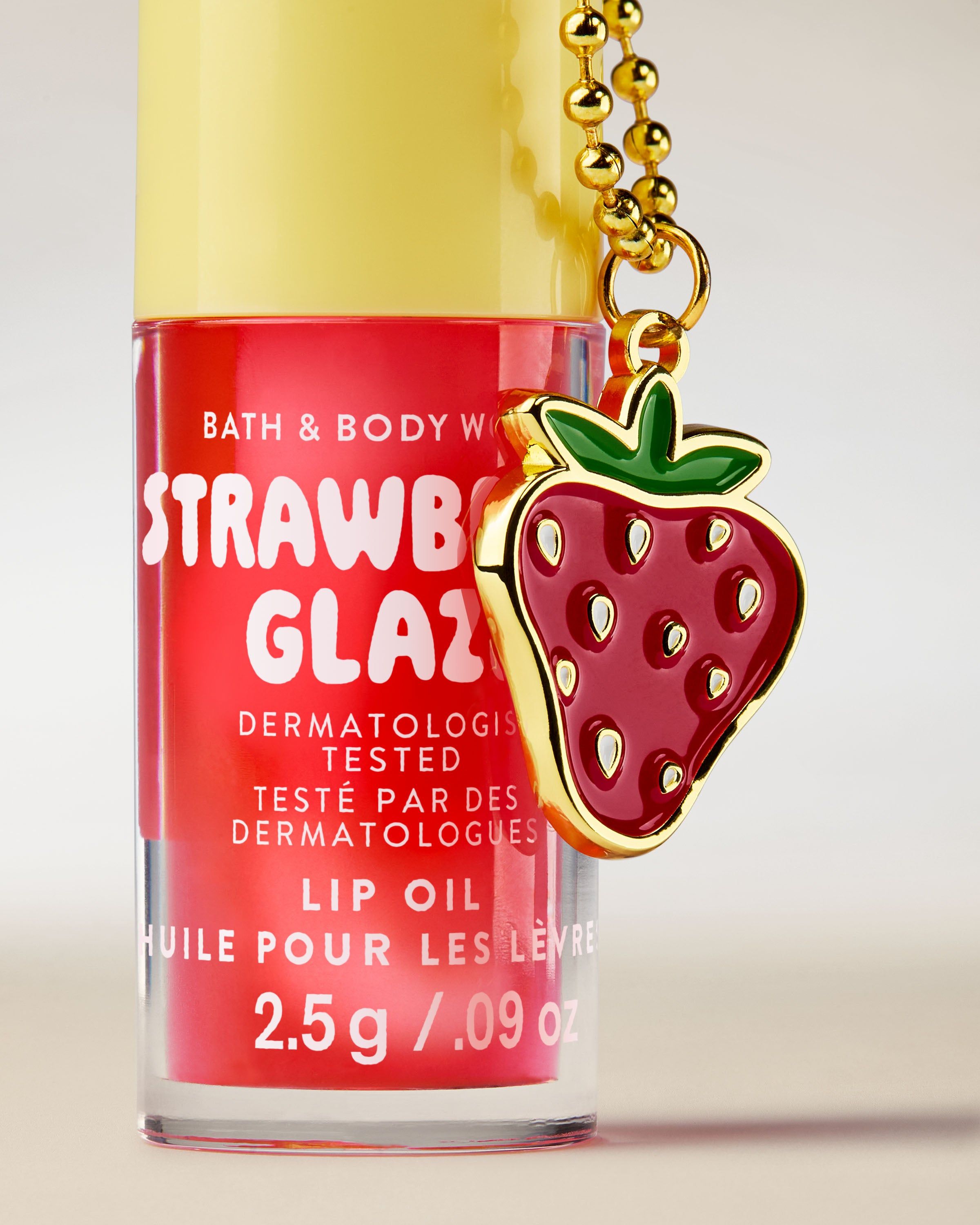 Ulei de buze Bath & Body Works Strawberry Glaze 2,5 g, în ambalaj roz cu breloc în formă de căpșună.