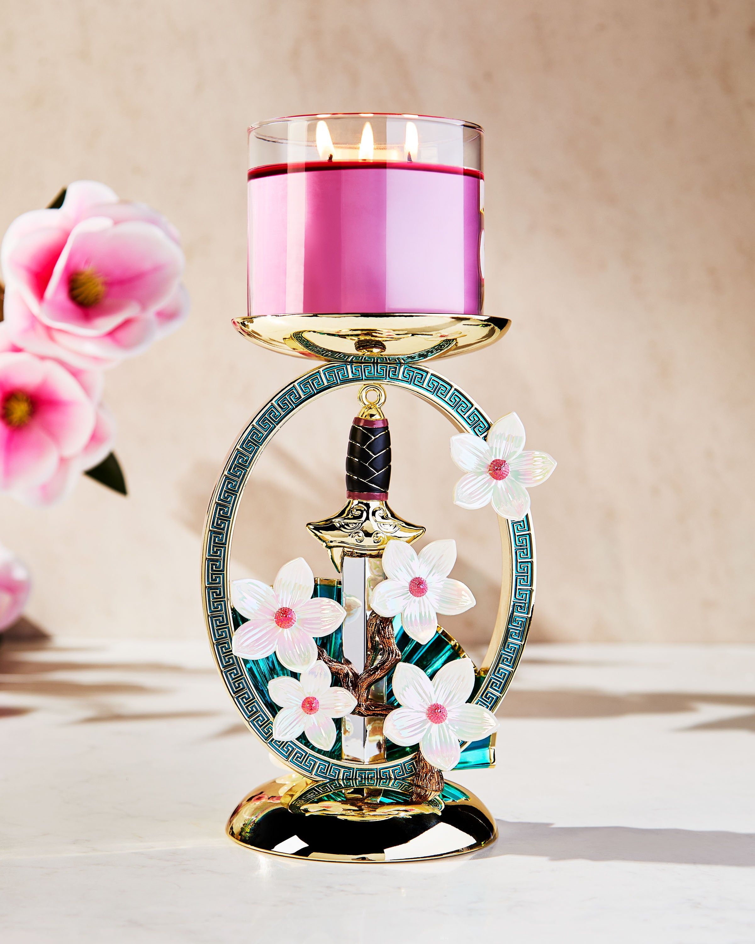 Suport Mulan pentru lumânare cu 3 fitiluri, cu sabie aurie, evantai și flori de magnolie într‑un cadru decorativ.