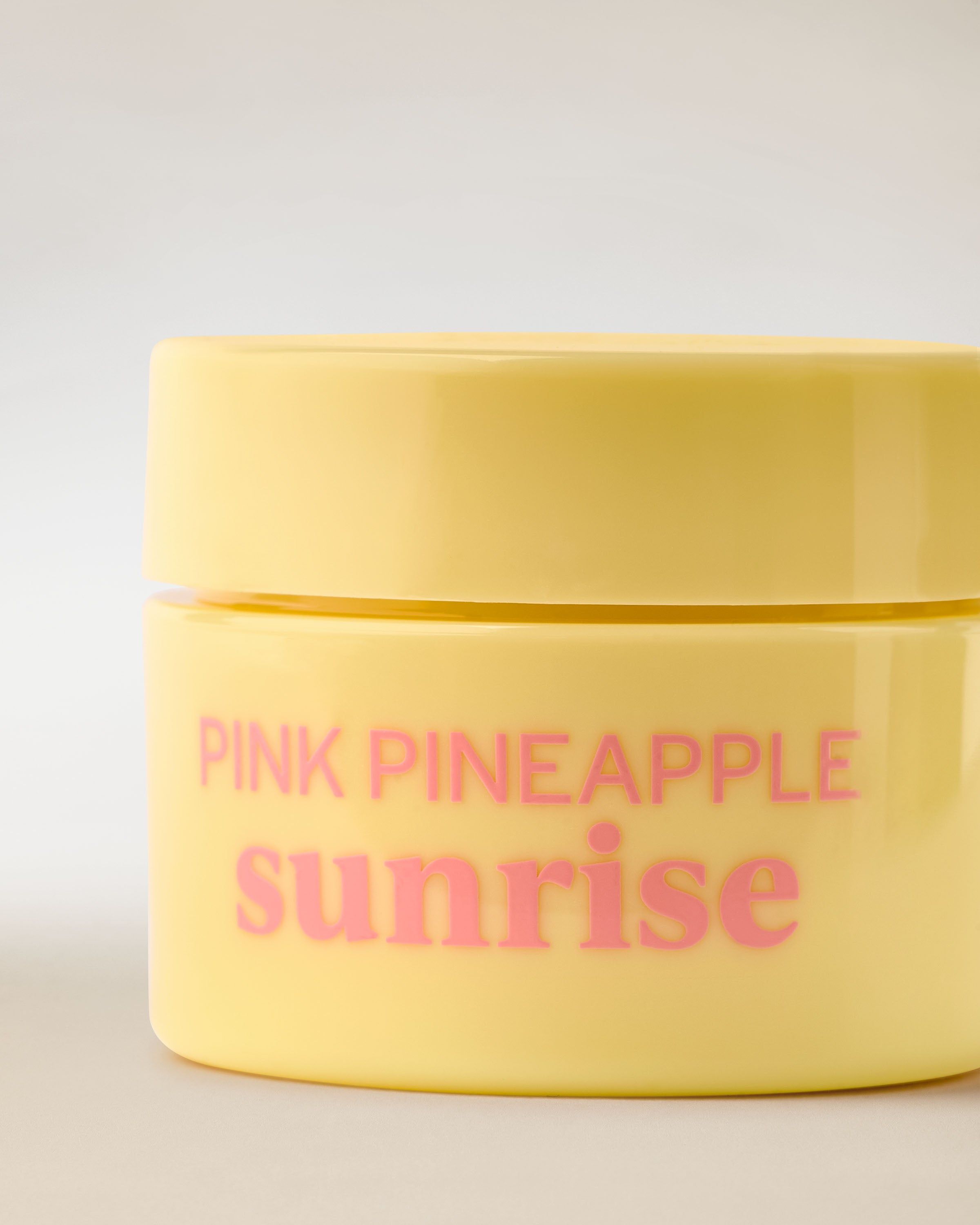 Borcan galben cu Nourishing Lip Mask, etichetă roz și detalii cu ananas, prezentat în cadru produs.