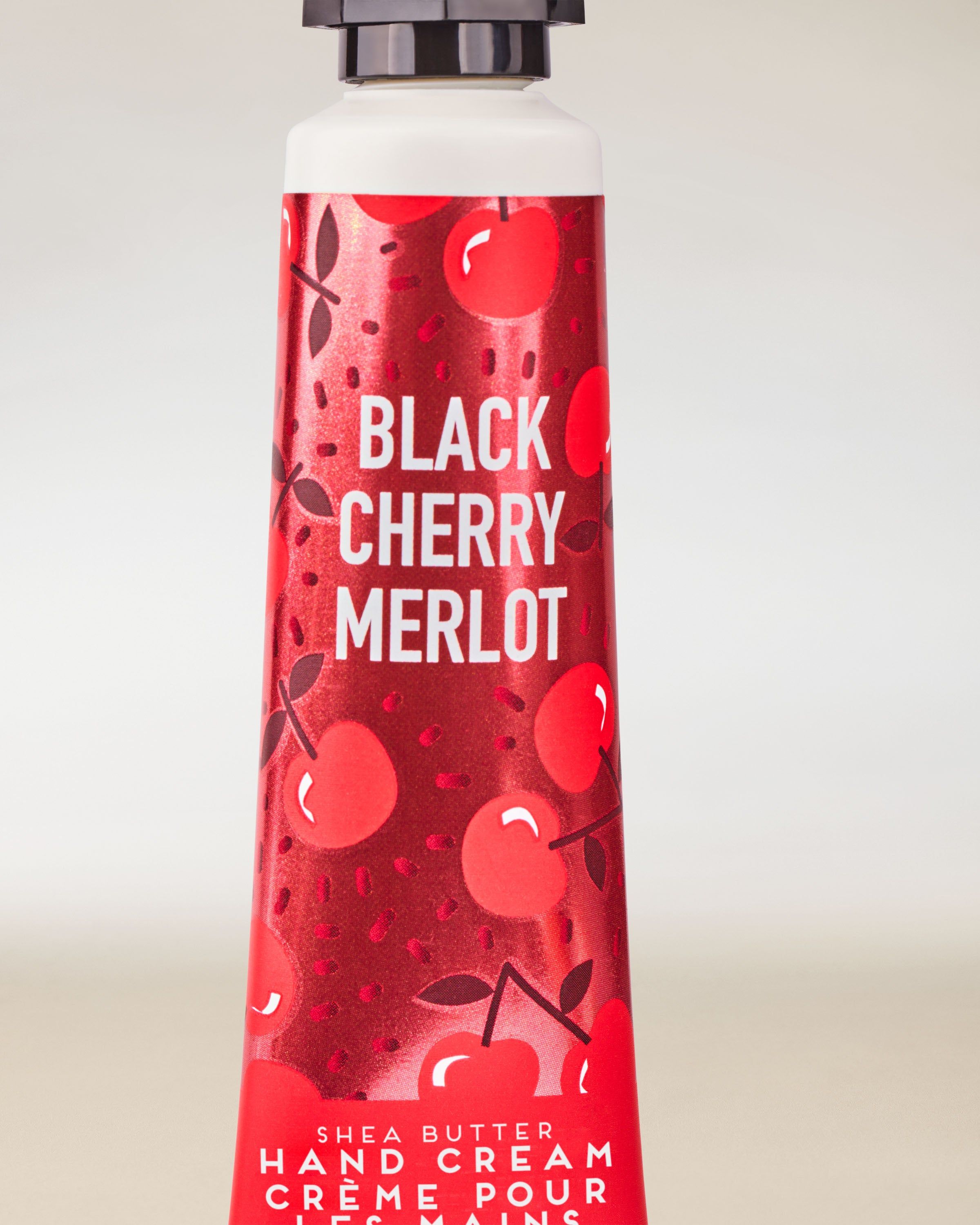 Cremă de mâini Black Cherry Merlot de la Bath & Body Works, tub roșu cu grafică decorativă cu cireșe.